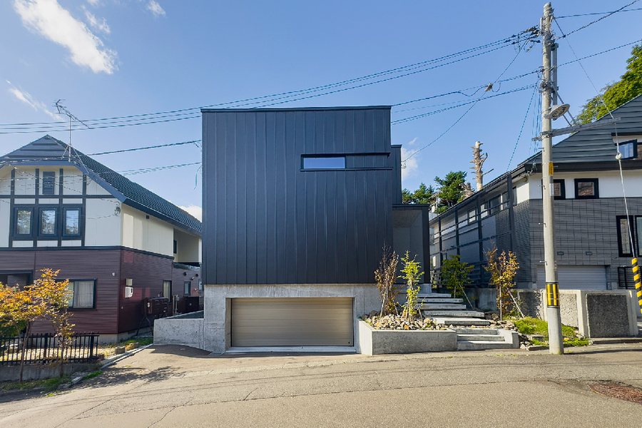 ビルトインガレージに艶消しのガルバリウム鋼板、光る階段。季節を感じさせる前庭が、訪れる人に穏やかな時間を演出する。