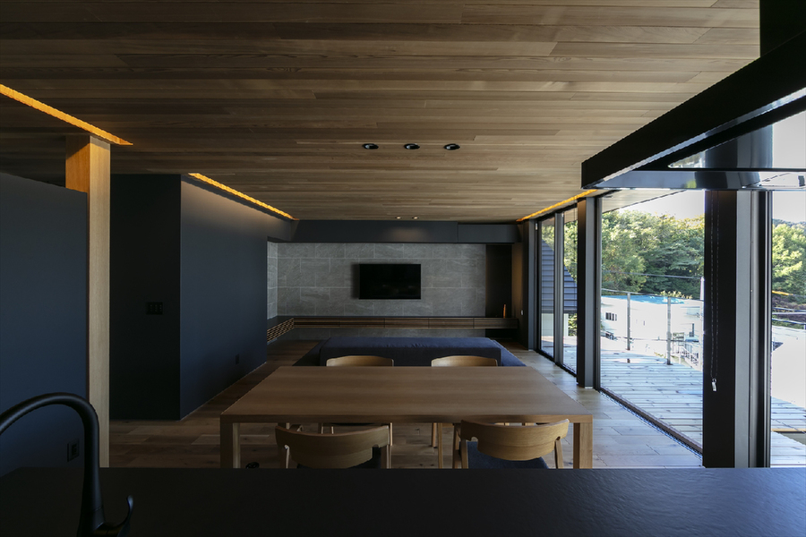 キッチンからは壁かけのテレビや寛ぐ人の姿、山景色に繋がるバルコニーが視界に広がる。